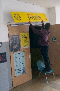 Eine Person, die gerade ein gelbes Schild mit der Aufschrift Pupille über eine Tür hängt
